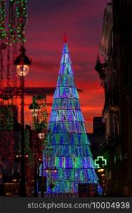 Illuminated Christmas tree rising in the center of the Puerta del Sol square in Madrid at dusk.
