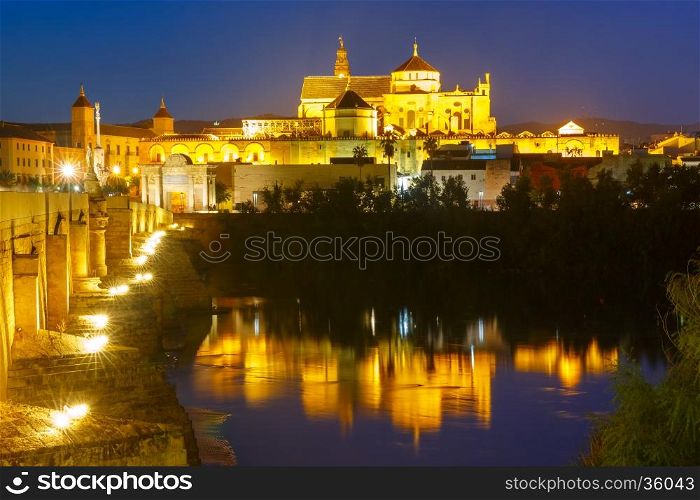 Illuminated Great Mosque Mezquita - Catedral de Cordoba with mirror reflection and Roman bridge across Guadalquivir river, Cordoba, Andalusia, Spain