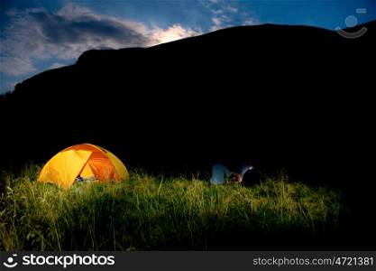 Illuminated orange camping tent on a field at sunset
