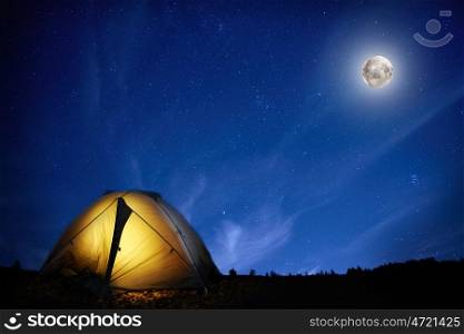 Illuminated orange camping tent under moon and stars at night