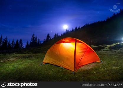 Illuminated orange camping tent under moon, stars at night