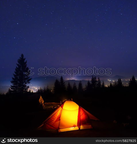 Illuminated orange camping tent under moon, stars at night