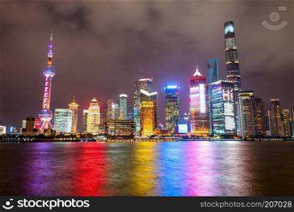Illuminated Shanghai city skyline at night, with colorful lights reflecting on water surface