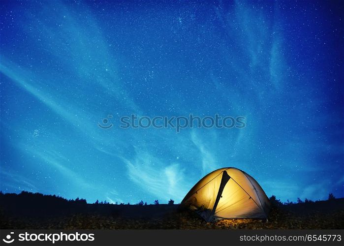 Illuminated yellow camping tent under stars at night. Illuminated yellow camping tent