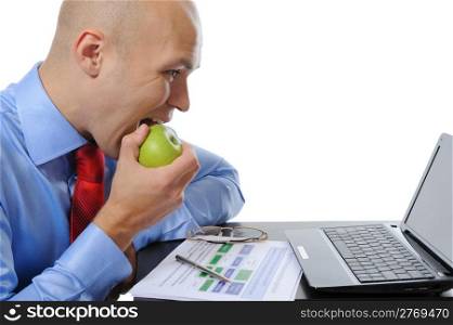 Image of a businessman in an office at the computer eating a green apple. Isolated on white background