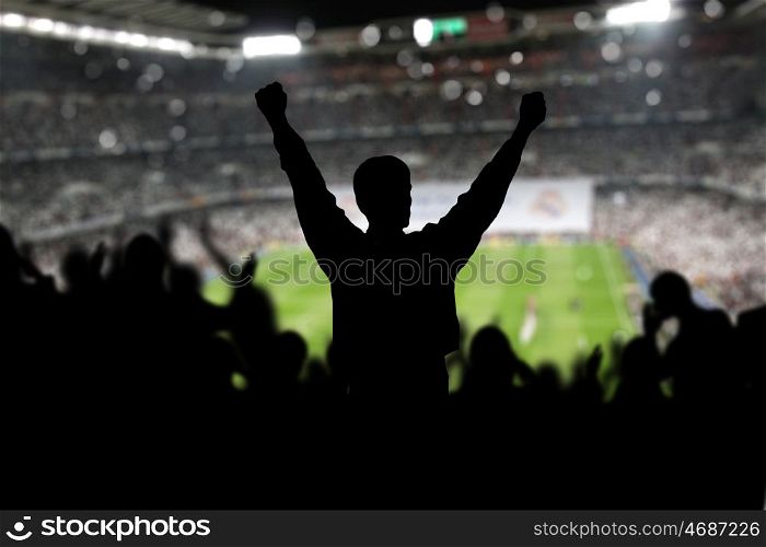 Image of a full stadium with silhouettes of fan on the foreground