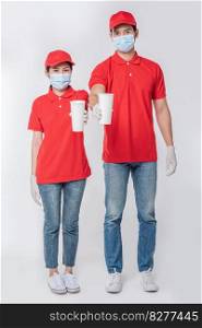 Image of a happy young delivery man in red cap blank t-shirt uniform face mask gloves standing with empty white paper cup isolated on light gray background studio, Service during pandemic coronavirus virus covid-19 concept