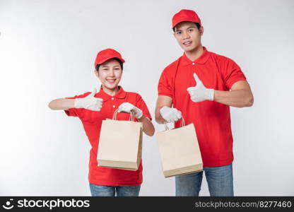 Image of a happy young delivery man in red cap blank t-shirt uniform standing with empty brown craft paper packet isolated on light gray background studio