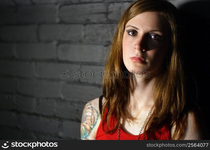 Image of a serious girl with upper arm tattoo. Harsh lighting for more dramatic effect.