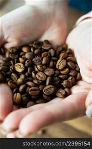 Image of a woman holding a roasted coffee bean in her hands, close-up, top view. The concept of making coffee. Image of a woman holding a roasted coffee bean in her hands, close-up, top view. The concept of making coffee.