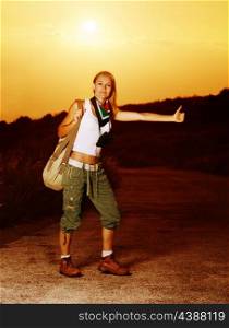 Image of active sporty girl traveling hitchhike, blond woman on road waiting for car, tourist female standing on highway with raised hand and stop auto, conceptual of vacation, adventure&#xA;