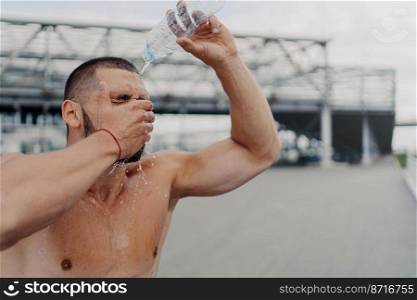 Image of athletic guy with muscular body pours water on himself from bottle, recovers after hard workout, feels tired and thirsty, cools body with cold liquid, loves sport. Healthy lifestyle