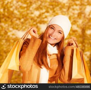 Image of attractive cheerful woman with brown shopping bags on golden autumn background, closeup portrait of happy female enjoying gift bags, spending money concept, sales season &#xA;&#xA;