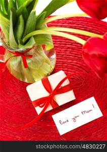 Image of beautiful romantic still life for mothers day, fresh red tulip flowers in glass vase, cute small white gift box with silk ribbon decoration, greeting card, love you mom, spring holiday&#xA;