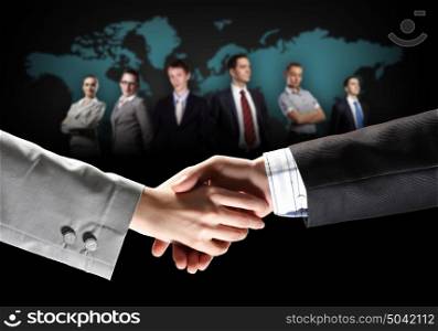 image of business handshake. business handshake against black background and standing businesspeople