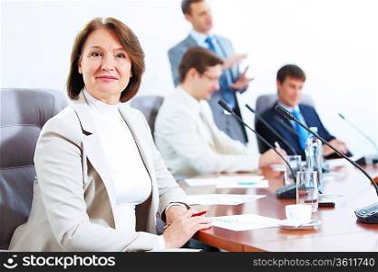 Image of businesswoman at business meeting with three businessmen in background
