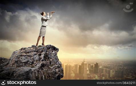Image of businesswoman looking in telescope standing a top of rock