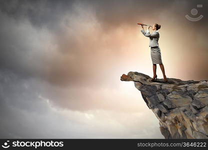 Image of businesswoman looking in telescope standing atop of rock