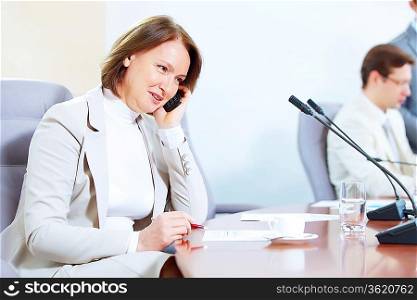 Image of businesswoman talking on mobile phone at business meeting with two businessmen in background