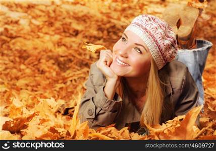 Image of cheerful teen laying down on the ground covered dry autumnal foliage in beautiful park, cute female wearing stylish colorful beret, autumn season, fall vacation, fun and joy concept