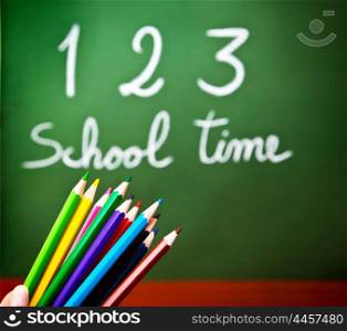 "Image of colorful pencils and green chalkboard with selective focus, multi colors crayons in preschool, handwriting phrase "school time" on blackboard in classroom, education and knowledge concept"