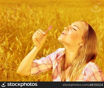 Image of cute blond girl blowing soap bubbles on wheat field, happy teenager having fun on golden crop meadow, closeup portrait of pretty young woman playing game on farm land, autumn season