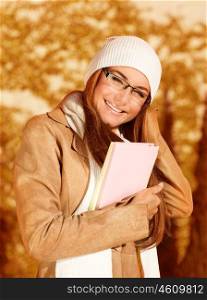 Image of cute businesswoman holding folder with documents, beautiful student girl wearing warm hat and scarf with elegant glasses, smart young lady enjoying autumnal educational period