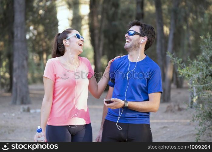 Image of excited man and woman with headphones listening to music on cell phones in the park