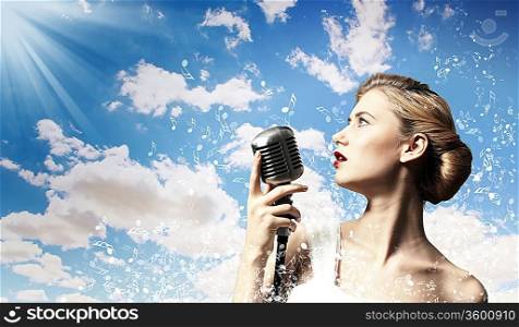 Image of female blonde singer holding microphone against clouds background
