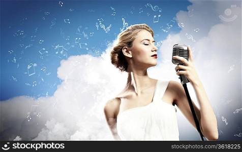 Image of female blonde singer holding microphone against clouds background with closed eyes