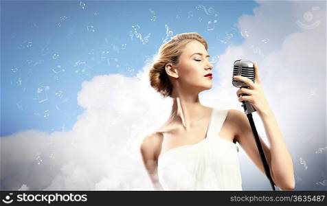 Image of female blonde singer holding microphone against clouds background with closed eyes