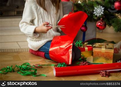 Image of girl sitting under Christmas tree and cutting wrapping paper
