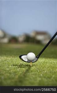 Image of golf ball on tee with golf club behind ball.