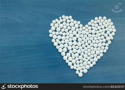 Image of heart made up out of white tablets on the blue background