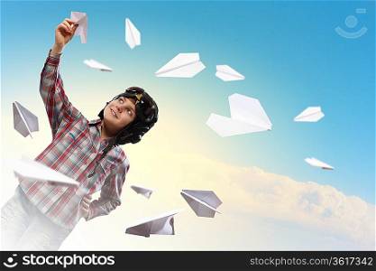 Image of little boy in pilots helmet playing with paper airplane