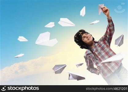 Image of little boy in pilots helmet playing with paper airplane