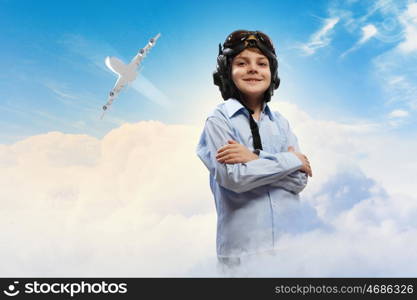 Image of little boy in pilots helmet with flying airplane in background