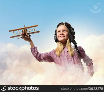 Image of little girl in pilots helmet playing with toy airplane against clouds background