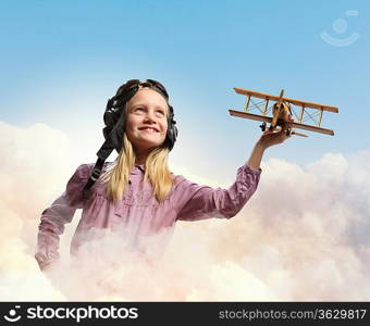 Image of little girl in pilots helmet playing with toy airplane against clouds background