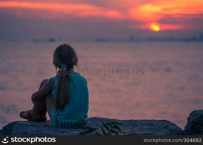 Image of little young girl sitting on the rock and looking the sunset. Image of little young girl sitting on the rock