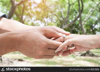 Image of man putting engagement ring to his girlfriend, outdoor in sunny day