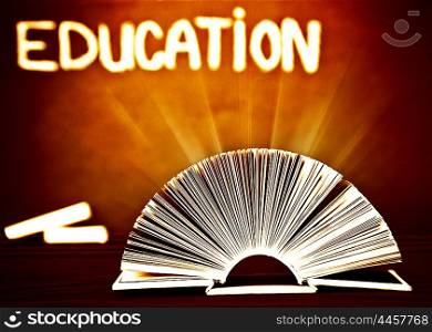 Image of open book on wooden school desk in classroom, textbook over brown chalkboard, magic book with glowing light, back to school, knowledge and education concept, retro style photo&#xA;&#xA;