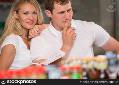 Image of positive couple choosing products in supermarket with list of things to buy