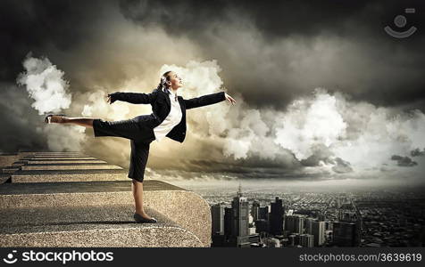 Image of pretty businesswoman balancing on the roof above cityscape