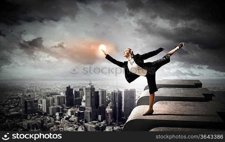 Image of pretty businesswoman balancing on the roof above cityscape