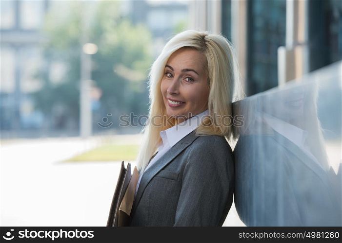 Image of pretty businesswoman looking at camera and holding documents outdoor