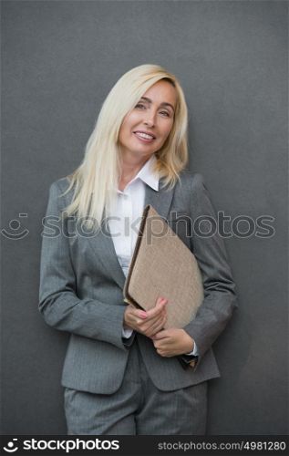 Image of pretty businesswoman standing near wall holding folder and looking away