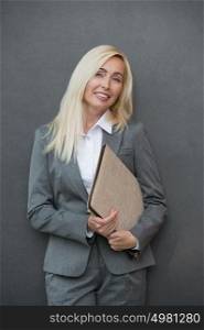 Image of pretty businesswoman standing near wall holding folder and looking away