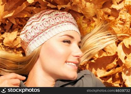 Image of pretty female laying down on old dry tree leaves, cute blond teenager having fun outdoors, attractive woman wearing warn beret, leisure time, relaxation outside, autumn season, sunny day