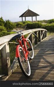 Image of red bike leaned up against railing of boardwalk.